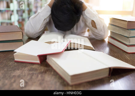confused and upset man with textbook stack on wooden desk in library Stock Photo