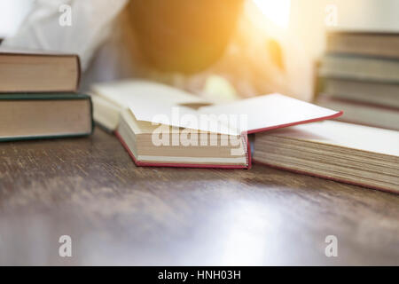confused and upset man with textbook stack on wooden desk in library Stock Photo