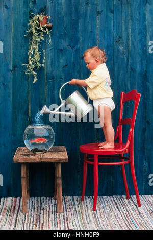 Three year-old girl pouring water in a goldfish bowl, Austria Stock Photo