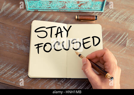 Retro effect and toned image of a woman hand writing a note with a fountain pen on a notebook. Handwritten text STAY FOCUSED as success and evolution  Stock Photo