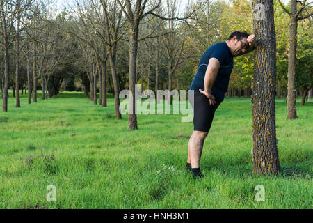 Abstract and conceptual tired, tired man in the woods. Man weighed down, resting after a run in the woods, leaning against a tree. Stock Photo
