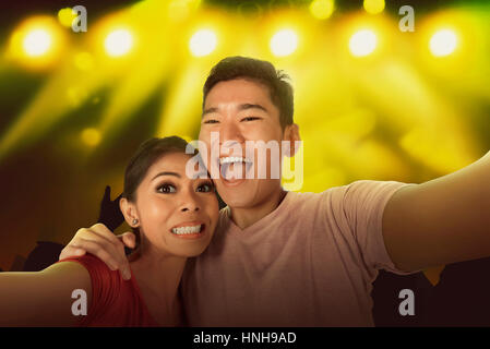 Young asian couple selfie with the crowd in front of bright stage lights Stock Photo