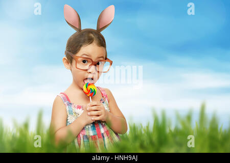 Portrait of a cute little girl dressed in easter bunny ears holding lollipop in the meadow Stock Photo
