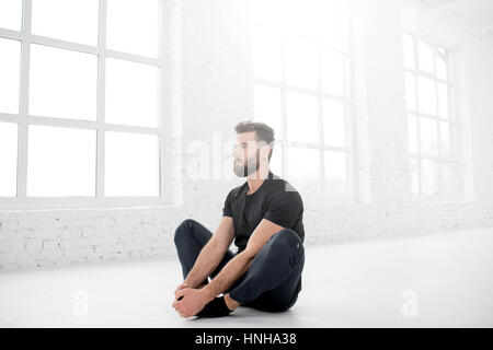 Handsome man in the black sportswear doing yoga in the white gym interior Stock Photo