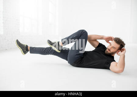 Handsome man in the black sportswear doing abs on the floor in the white gym interior Stock Photo