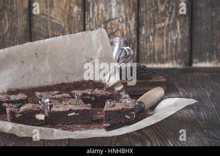 Homemade dark chocolate brownies with cream cheese on baking paper on rustic wooden table Stock Photo