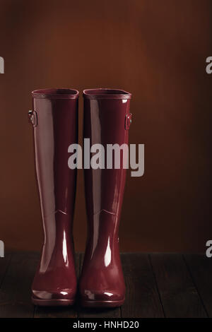 Photo in low key. Rubber boots burgundy color on a brown background. Selective focus. Stock Photo
