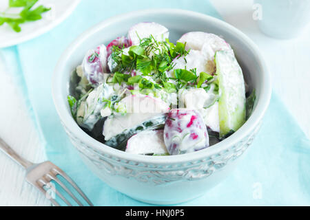 Healthy homemade creamy vegetable salad with greens over rustic wooden background - radish, potato, cucumber creamy salad for healthy spring or summer Stock Photo