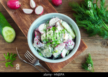 Healthy homemade creamy vegetable salad with greens over rustic wooden background - radish, potato, cucumber creamy salad for healthy spring or summer Stock Photo