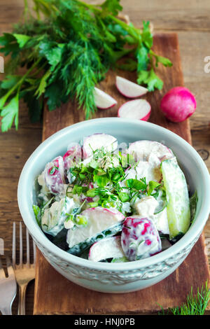Healthy homemade creamy vegetable salad with greens over rustic wooden background - radish, potato, cucumber creamy salad for healthy spring or summer Stock Photo