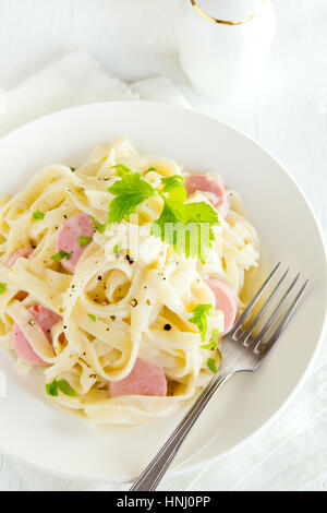 Alfredo tagliatelle pasta with sausages, creamy sauce and greens on white plate - homemade creamy pasta Stock Photo
