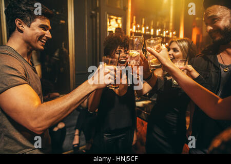 Group of men and women enjoying drinks at nightclub. Young people at bar toasting cocktails and laughing. Stock Photo
