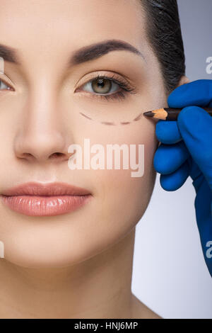 Plastic surgeon drawing dashed line under eye Stock Photo