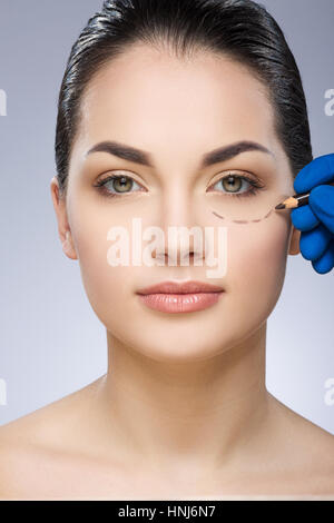 Plastic surgeon drawing line under eye Stock Photo