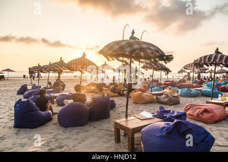 BALI, INDONESIA - OCTOBER 31, 2015: Tourists enjoy a drink while watching the sunset in a beach bar along Seminyak beach, just north of Kuta, in Bali. Stock Photo