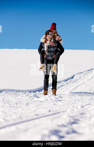 Couple playing in snow. Man giving woman piggyback ride on winter vacation. Stock Photo