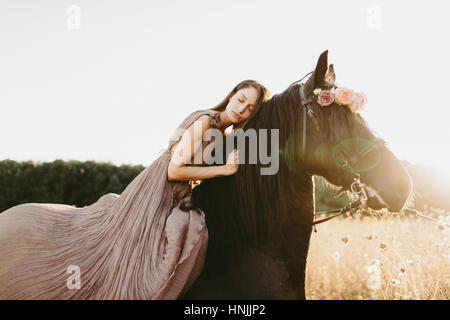 Caucasian woman wearing a beige flowy dress sitting on a black horse, dreaming, contemplating Stock Photo