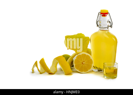 Open glass decanter bottle and shot glass filled with yellow lemon liquor or limoncello or limoncino on white. Peeled natural organic lemon. Stock Photo
