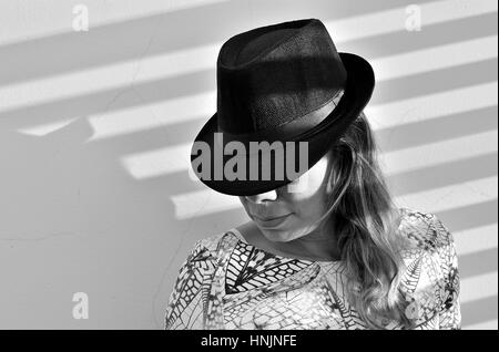 Woman hidding her face with a hat in front of a wall Stock Photo