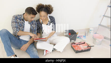After long day of painting young couple sit by ladder and pail while discussing colors Stock Photo