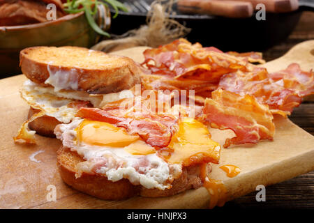 Sandwich with fried egg and hot bacon pieces on wooden background Stock Photo