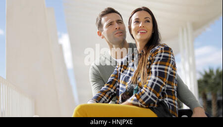 Low angle view of an attractive trendy young woman with her boyfriend looking into the distance with a smile as they watch something off frame Stock Photo