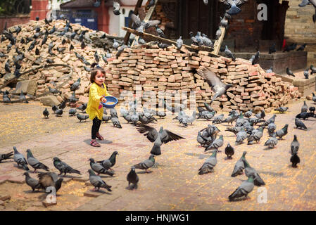 A little girl feeds a flock of doves near the ruins of ancient temple in Kathmandu, Nepal. Stock Photo