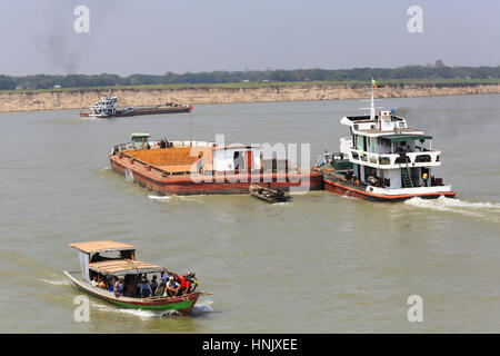 Local passenger ferry and tug and barge traffic on the Irrawaddy River in Myanmar (Burma). Ferry passengers are taking photos of river cruise boat. Stock Photo