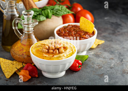 Homemade hummus and tomato salsa in white bowls with vegetables and corn chips Stock Photo
