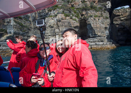 Chinese tourists taking selfies on Pennicott Wilderness Journey's cruise of the Tasman Peninsula's coastline in Tasmania. Stock Photo