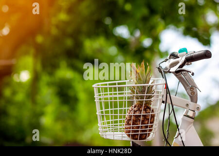 Pineapple in bike basket on green blurred background bokeh. Soft orange light effect. Stock Photo