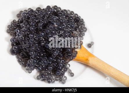 top view of black coloured pickled caviar of halibut fish in wooden spoon on white plate Stock Photo