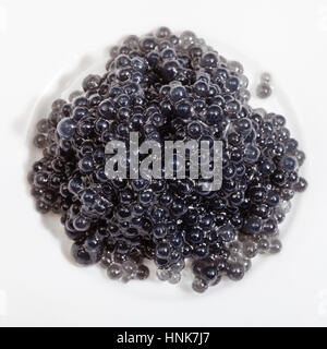 top view of black dyed salty caviare of halibut fish on white plate Stock Photo