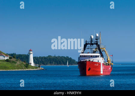 Canadian Coast Guard Ship (CCGS) 'Alfred Needler' passes a lighthouse while entering Halifax Harbour, Nova Scotia, Canada. Stock Photo