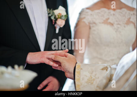 Priest puts wedding ring at grooms hand at church. Stock Photo
