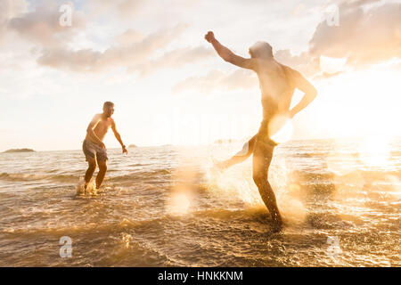 Two people having fun fighting with water splash in the sea with summer sunset, droplets effect and tilted photo to show action Stock Photo
