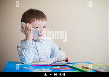 little boy sitting at desk and talking on the phone Stock Photo