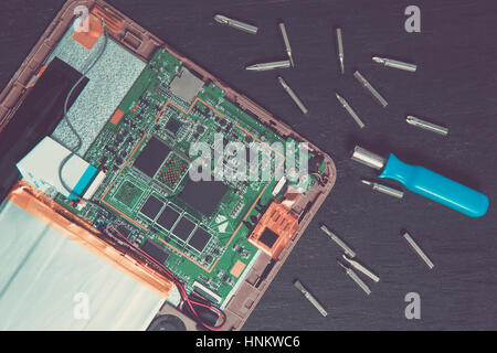 Process of PC Tablet device repair near screwdriver and bit on black wooden background. Top view. Stock Photo