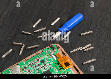 Process of PC Tablet device repair near screwdriver and bit on black wooden background. Disassembled. Stock Photo