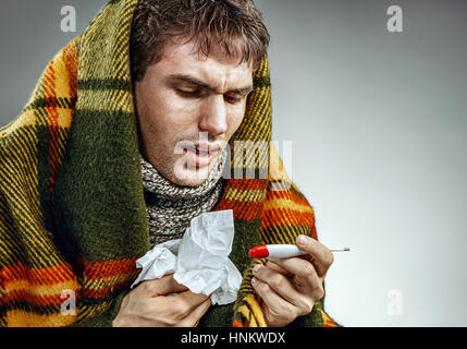 Ill man covered with plaid blanket holding tissue and thermometer. Photo of man suffering cold and winter flu virus Stock Photo