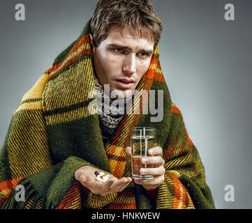 Sick man with tired face expression, taking medicine tablets. Photo of man suffering common cold and winter flu virus. Stock Photo