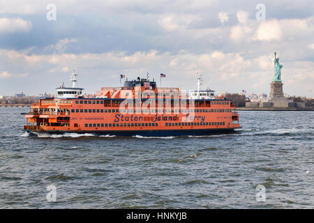 A Staten Island ferry crosses the upper New York harbour passing the Statue of Liberty as it makes its way towards Manhattan across the Hudson River Stock Photo
