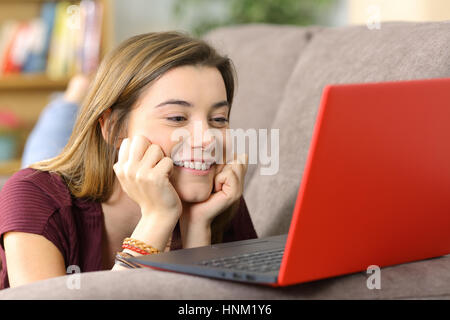 Candid teen watching media content on line in a colorful laptop lying on a sofa in the living room at home Stock Photo