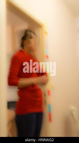 Blurred abstract view of a woman with red clothes standing in a room touching her chin Stock Photo