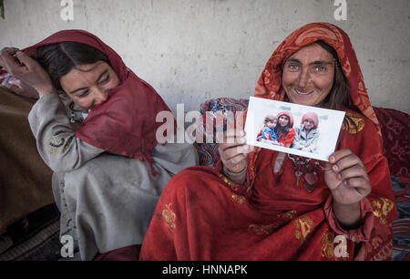 Afghanistan, Wakhan corridor,a family at home, old woman showing a family photo,two kids near to her, dressed in traditional ethnic clothes. Stock Photo