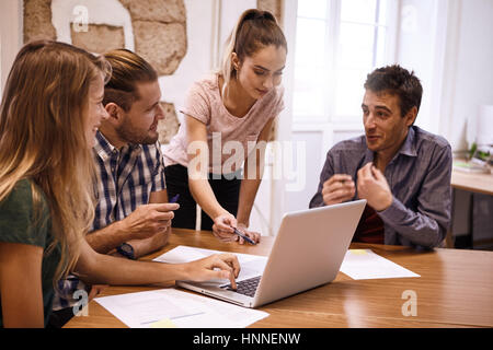Young business team in lively discussion during a meeting with a presentation on a laptop and note paper on the table between them Stock Photo