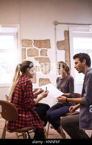 Creative team of three energetic young business people sitting together sharing new thoughts and ideas around their business and where to take it Stock Photo