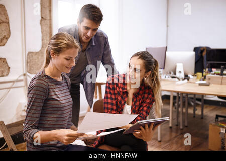 Team of three happy young professional business people sharing ideas and thoughts with a tablet and some notes Stock Photo