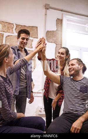 Four happy young people high fiving each other with one couple standing behind the other couple that is sitting down Stock Photo