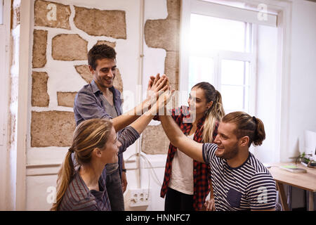 Team of your young business people giving the high five all with joyful and big happy smiles looking at each other feeling accomplished Stock Photo